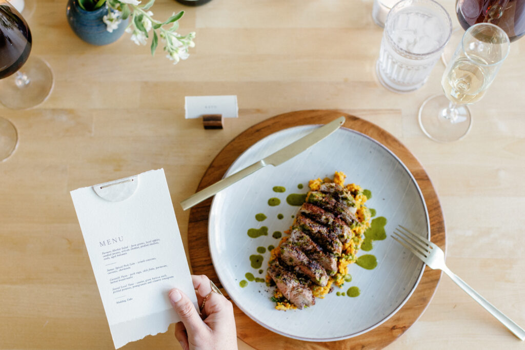 A beautifully plated dinner featuring a perfectly cooked steak topped with a savory glaze, accompanied by creamy mashed sweet potatoes garnished with fresh herbs, served on an elegant plate with a stylish menu card in the background.